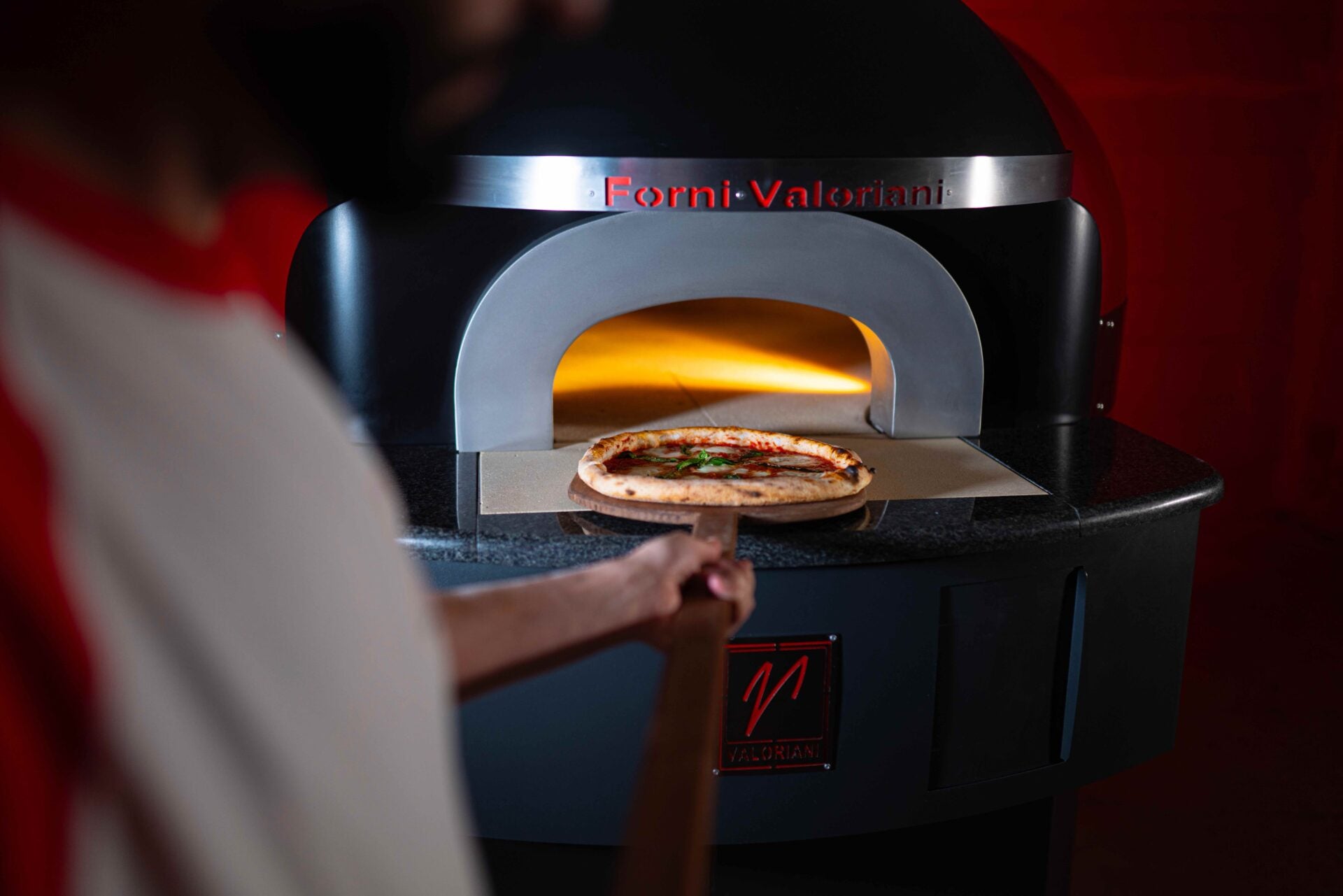 Direkt befeuerter Holz-Pizzaofen mit Flammen im Backraum am Gartenfest